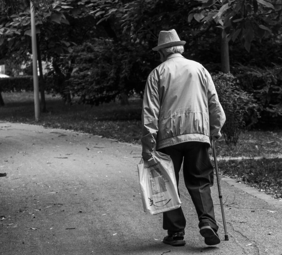 older man walking away, using a cane